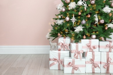 Photo of Beautiful decorated Christmas tree and gifts near pink wall. Space for text