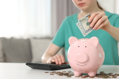 Financial savings. Woman putting dollar banknote into piggy bank at white wooden table indoors, closeup