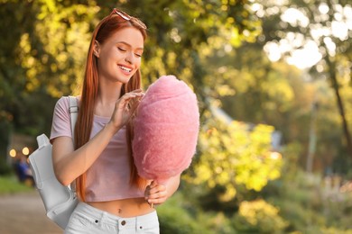 Photo of Smiling woman with cotton candy outdoors on sunny day. Space for text