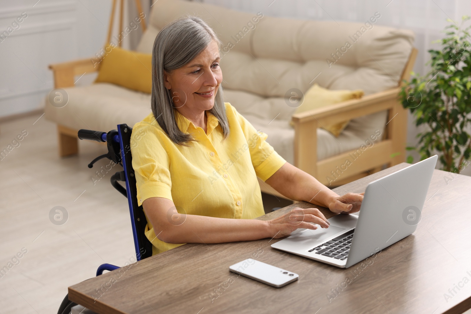 Photo of Woman in wheelchair using laptop at table in home office