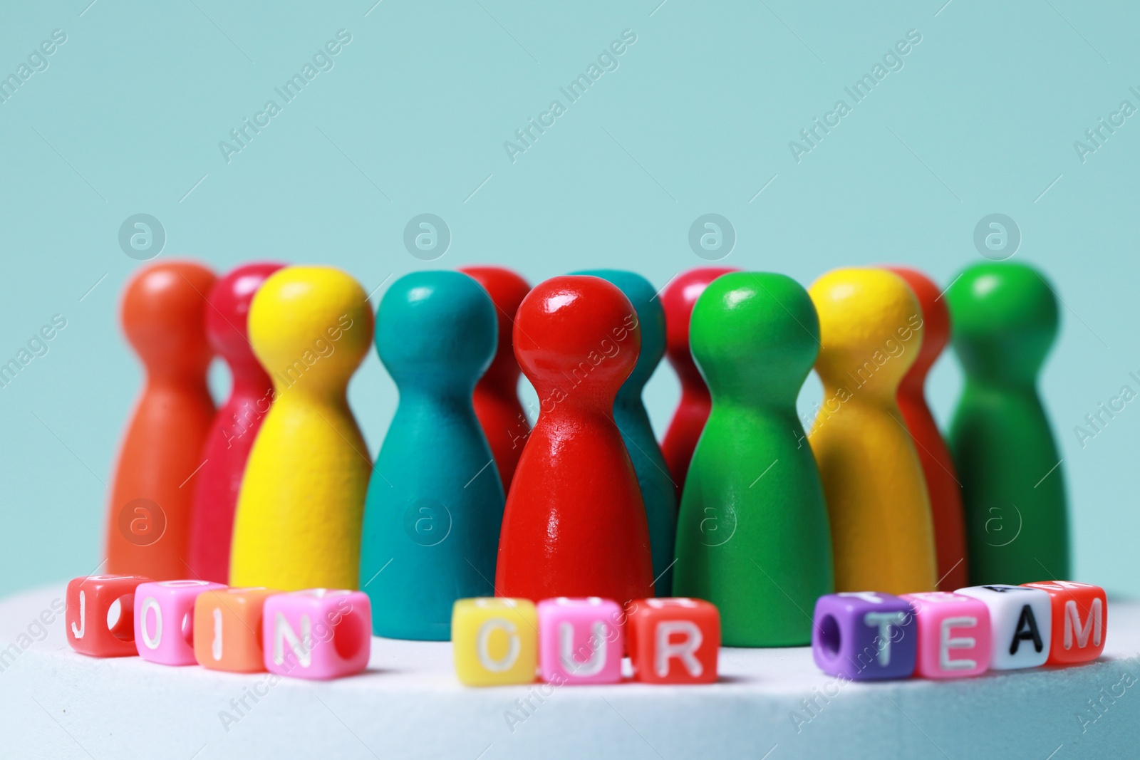 Photo of Colorful cubes with phrase Join Our Team and pawns on white round podium, closeup. Recruiter searching employee