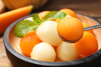 Scoop with melon ball near plate of fruit salad, closeup