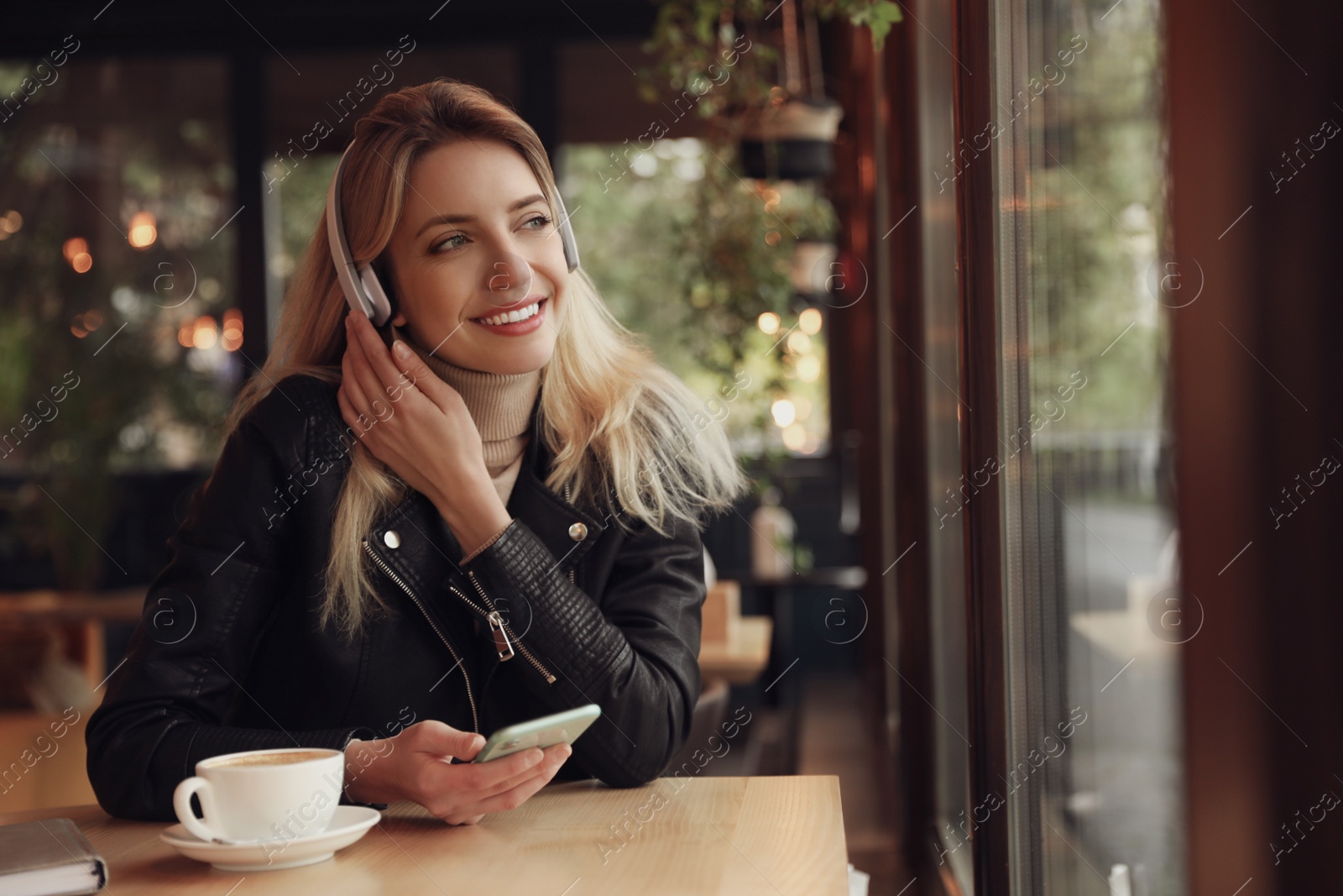 Photo of Young woman with headphones and smartphone listening to music in cafe