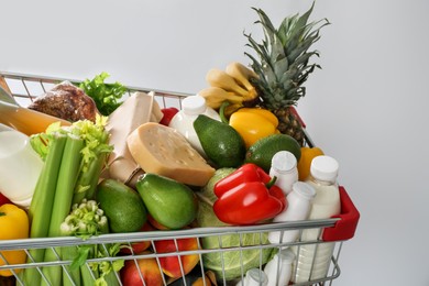 Photo of Shopping cart full of groceries on grey background, closeup