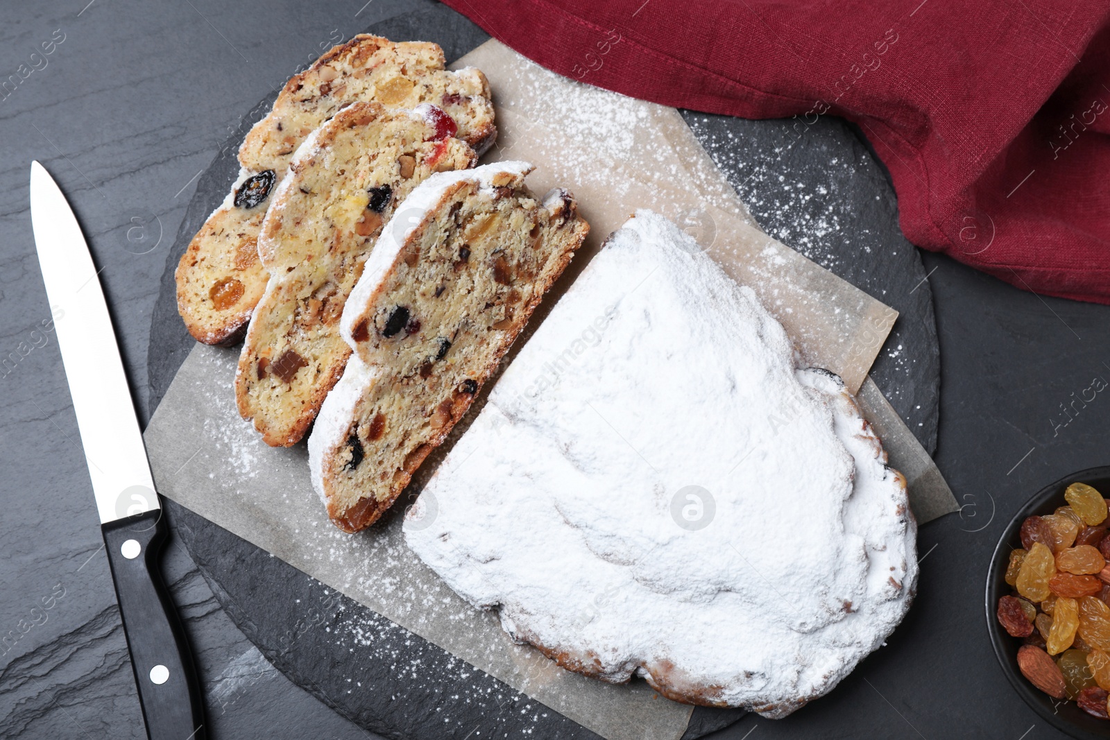 Photo of Traditional Christmas Stollen with icing sugar on black table, flat lay