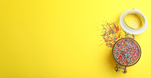 Photo of Colorful sprinkles in jar on yellow background, flat lay with space for text. Confectionery decor