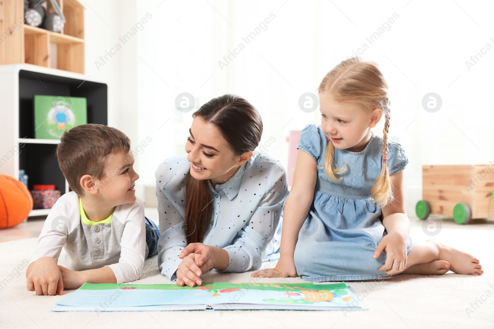 Photo of Kindergarten teacher reading book to children indoors. Learning and playing