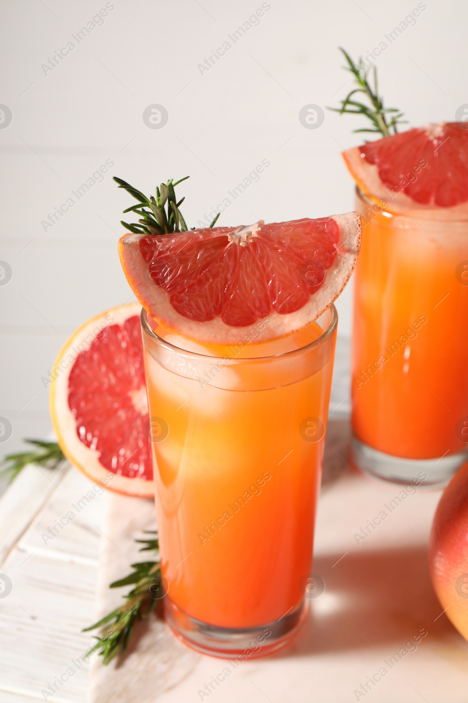 Photo of Tasty grapefruit drink with ice in glasses, rosemary and fresh fruits on light table