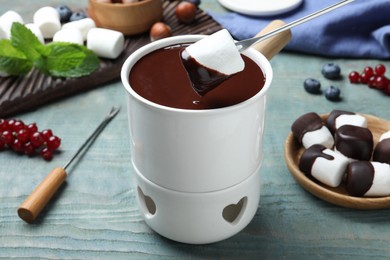 Photo of Dipping marshmallow into melted chocolate at blue wooden table, closeup