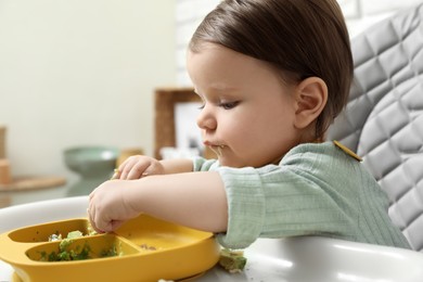 Photo of Cute little baby eating healthy food in high chair indoors