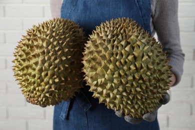 Photo of Woman holding fresh ripe durians near white brick wall, closeup