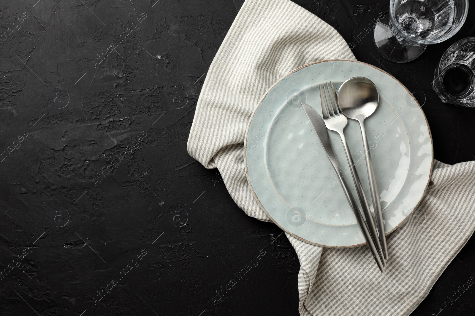 Photo of Stylish setting with cutlery, napkin and plate on dark textured table, flat lay. Space for text