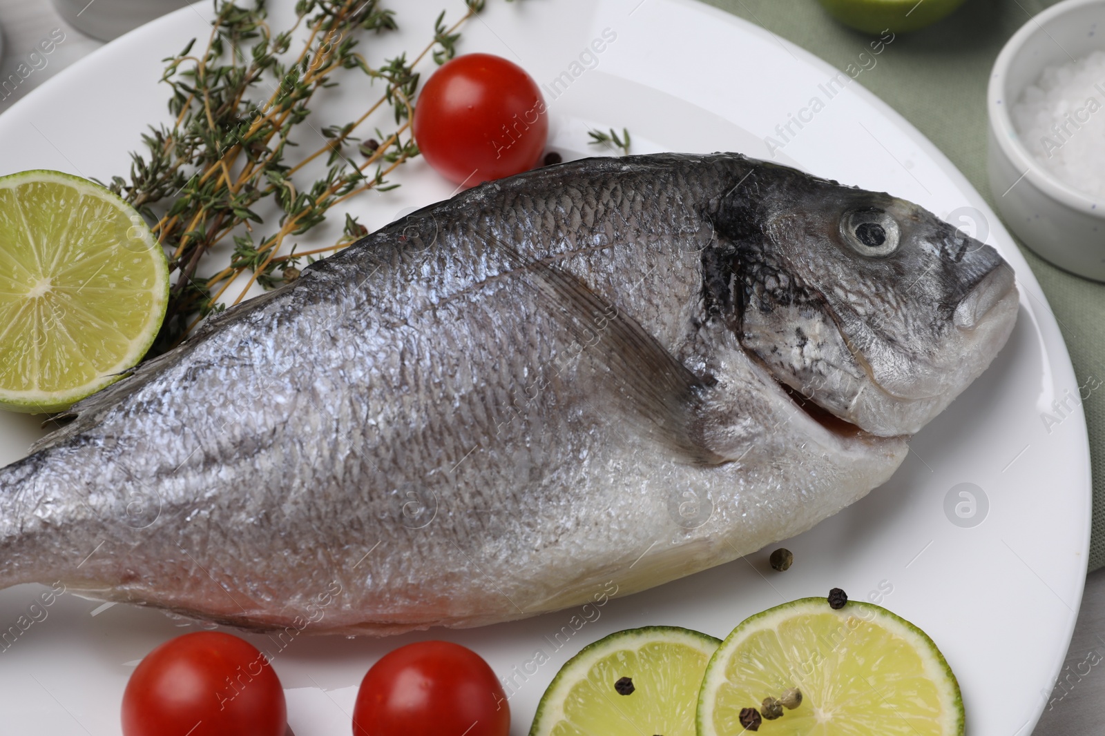 Photo of Raw dorado fish, lime slices, tomatoes and thyme on table, closeup