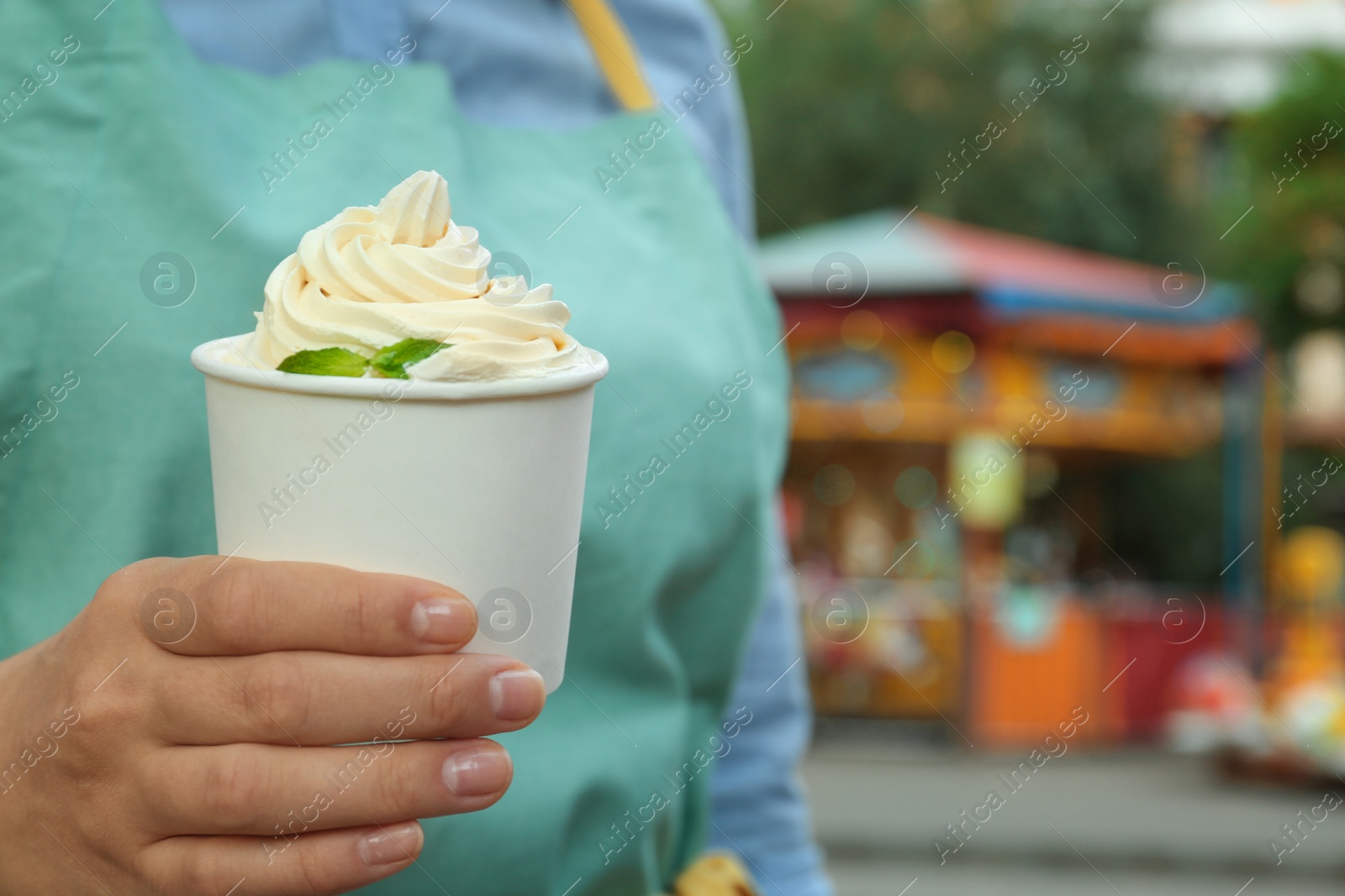 Photo of Woman holding cup with tasty frozen yogurt outdoors, closeup. Space for text