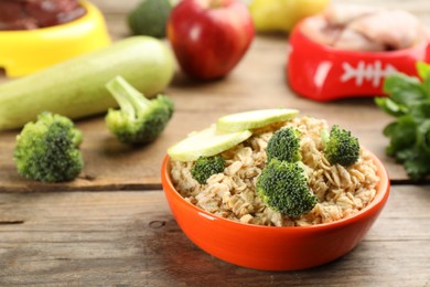Feeding bowl with oatmeal porridge and vegetables on wooden table, closeup. Natural pet food
