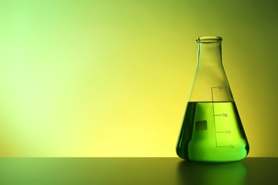 Conical flask with liquid on table against color background. Chemistry laboratory glassware