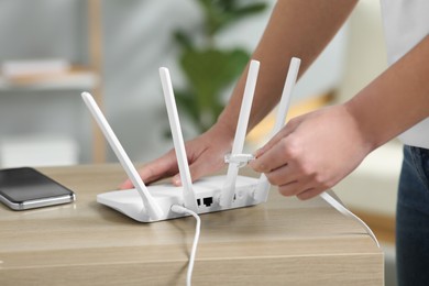 Photo of Woman inserting ethernet cable into Wi-Fi router at table indoors, closeup