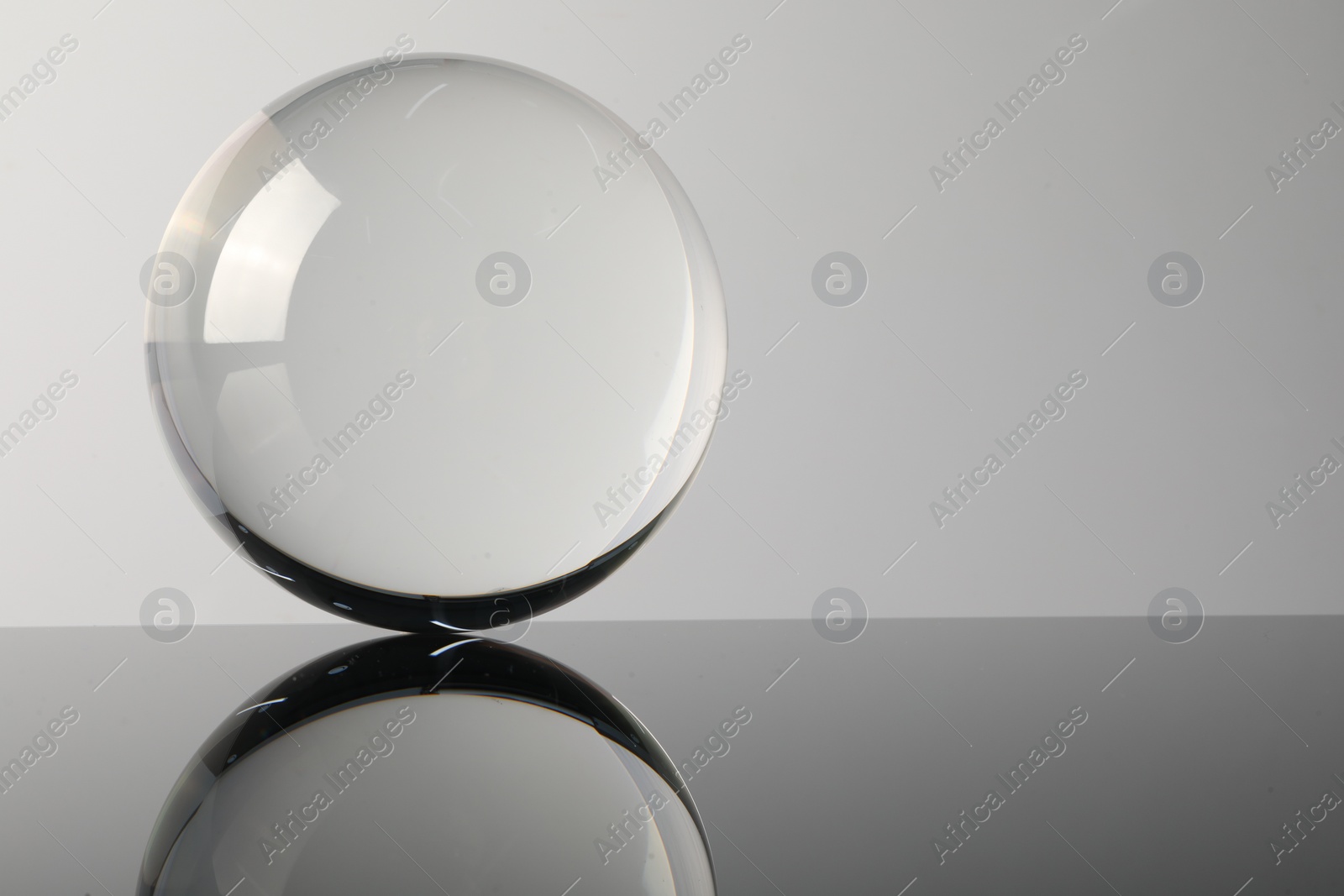 Photo of Transparent glass ball on mirror surface against light background. Space for text