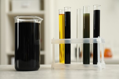 Photo of Laboratory glassware with different types of crude oil on light grey table