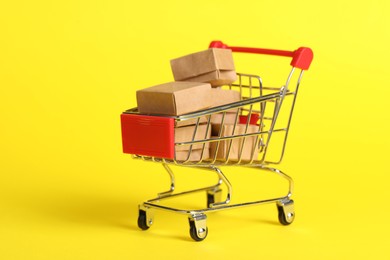 Photo of Small metal shopping cart with boxes on yellow background