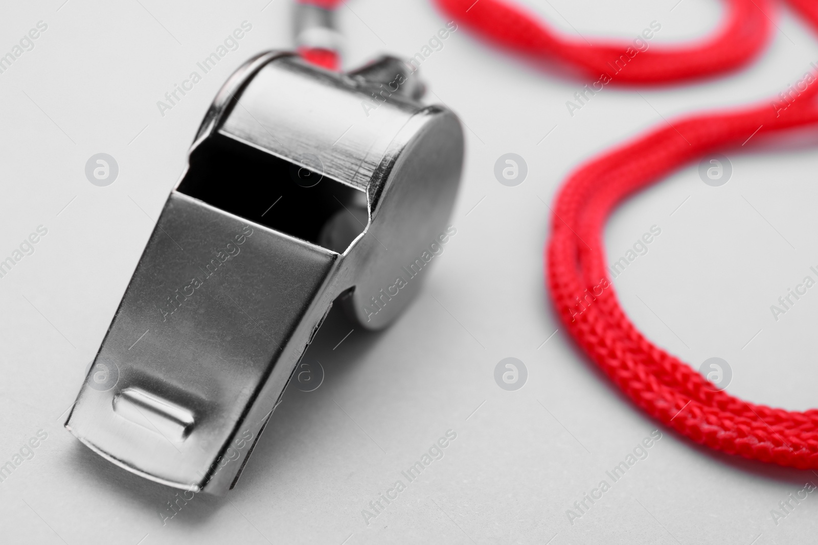 Photo of One metal whistle with red cord on white background, closeup