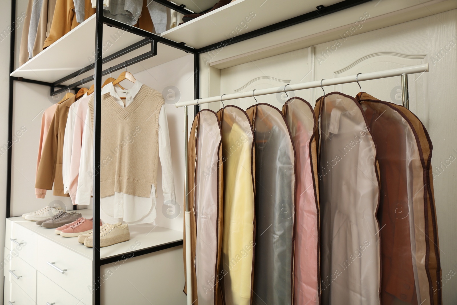 Photo of Garment bags with clothes on rack in dressing room