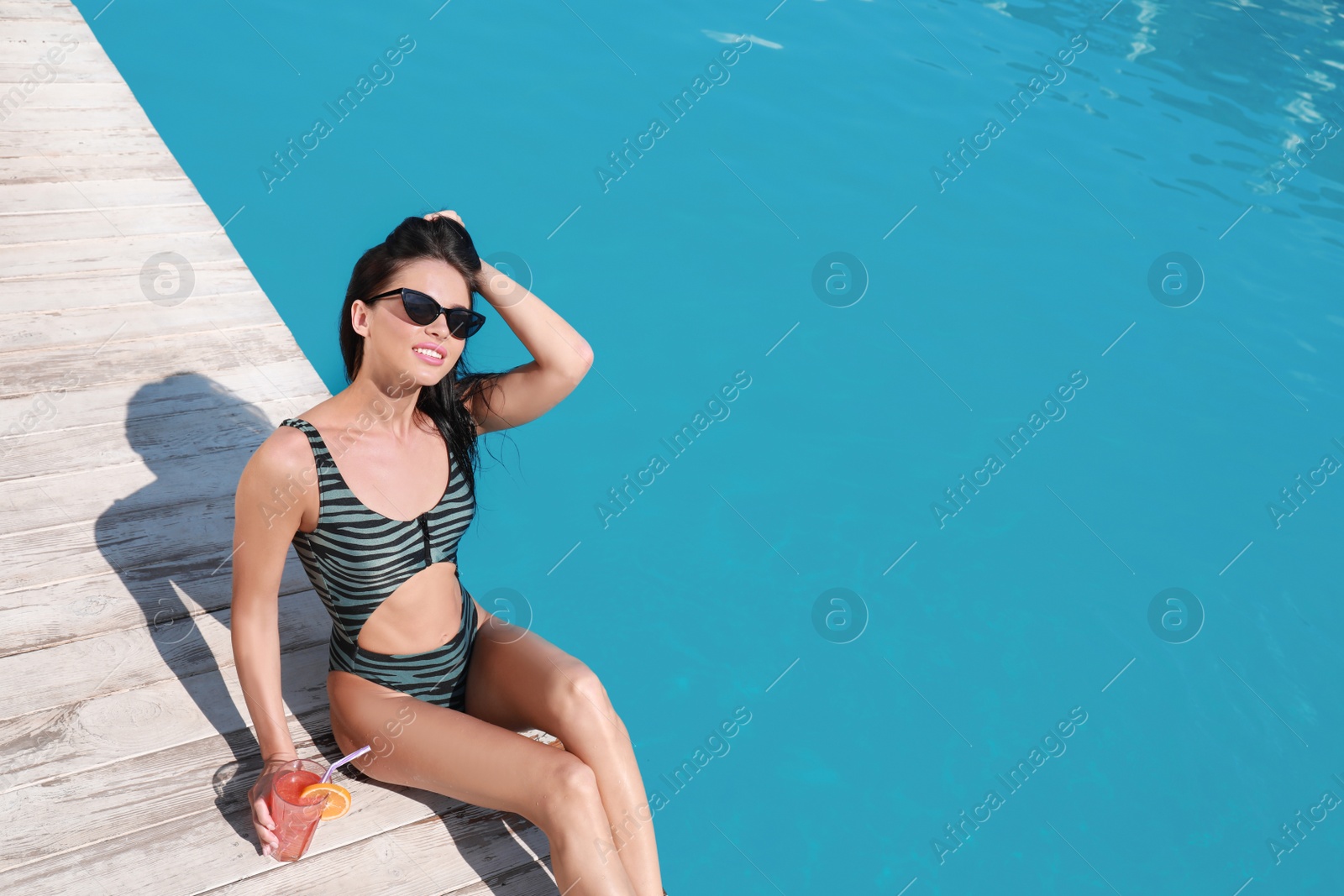 Photo of Beautiful young woman with refreshing cocktail near swimming pool on sunny day, above view