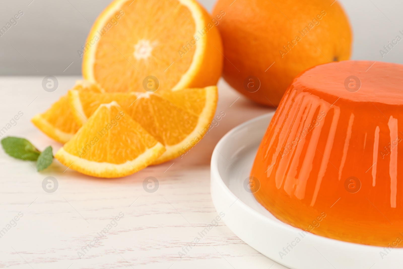 Photo of Plate with tasty jelly and oranges on white wooden table, closeup. Space for text