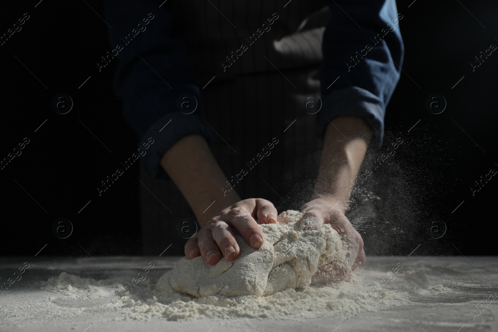 Photo of Making bread. Woman kneading dough at table on dark background, closeup