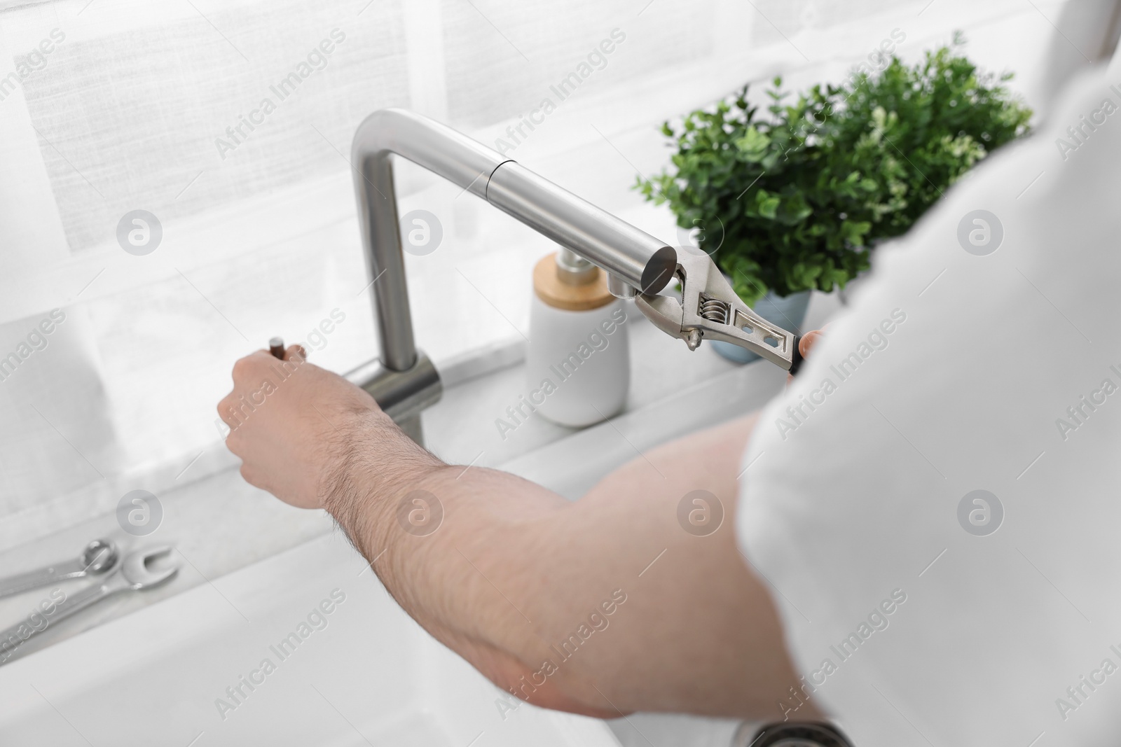 Photo of Plumber repairing faucet with spanner indoors, closeup