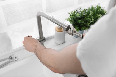 Plumber repairing faucet with spanner indoors, closeup