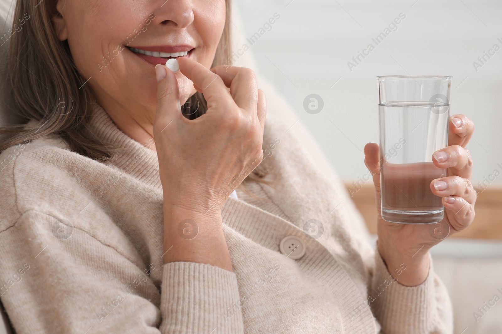 Photo of Senior woman with glass of water taking pill indoors, closeup