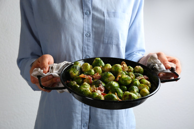 Photo of Woman holding wok with Brussels and bacon on light background, closeup