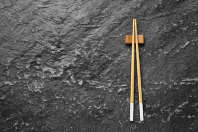 Photo of Pair of wooden chopsticks with rest on black textured table, top view. Space for text