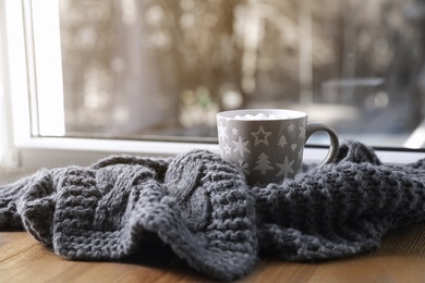 Photo of Cup of winter drink and knitted scarf on windowsill. Space for text