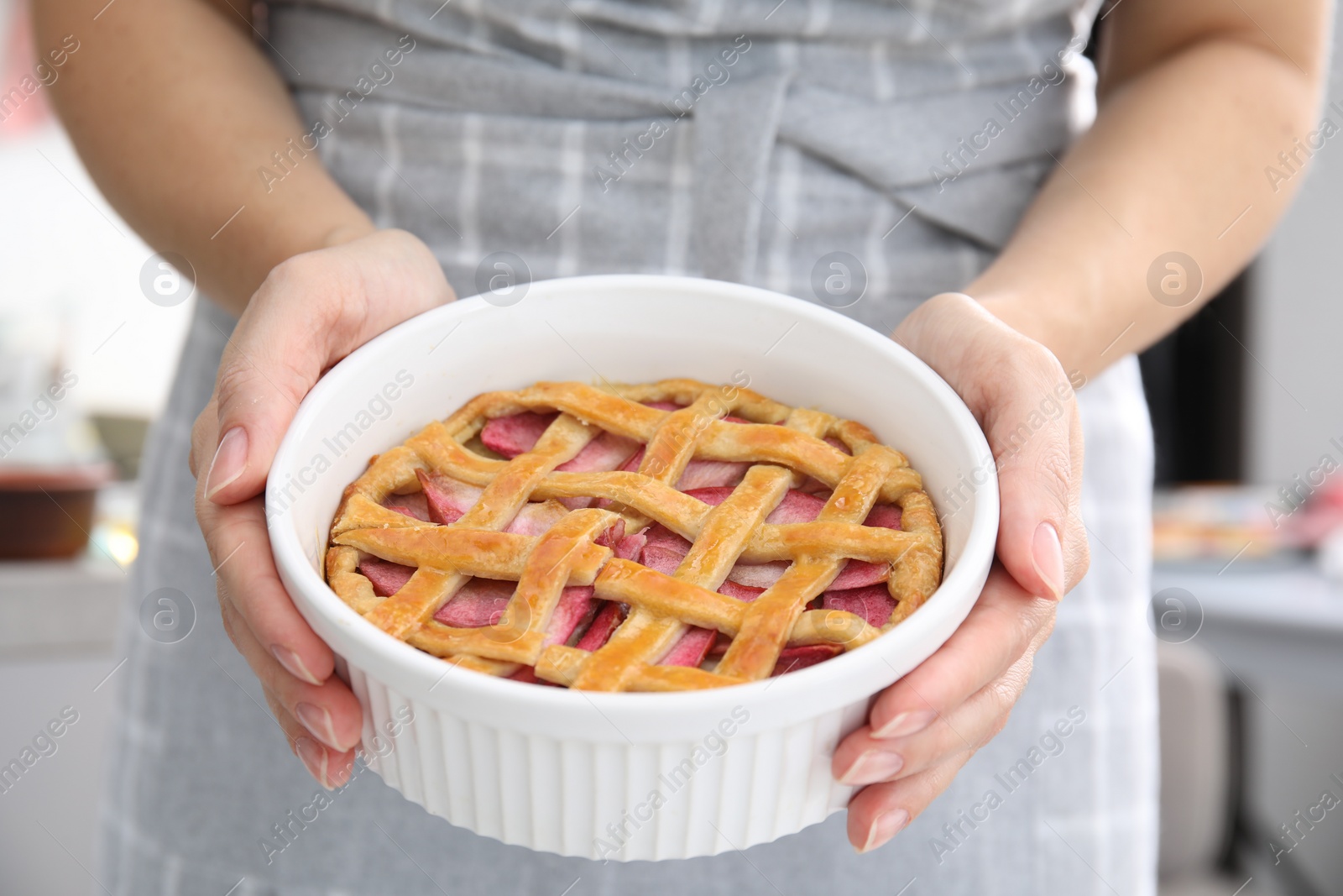Photo of Woman holding baking dish with delicious apple pie indoors, closeup