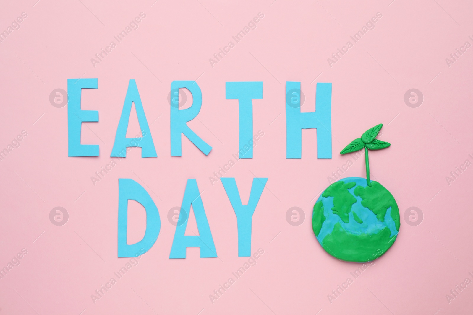 Photo of Phrase Earth Day and planet model with green seedling on pink background, flat lay