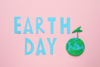 Photo of Phrase Earth Day and planet model with green seedling on pink background, flat lay