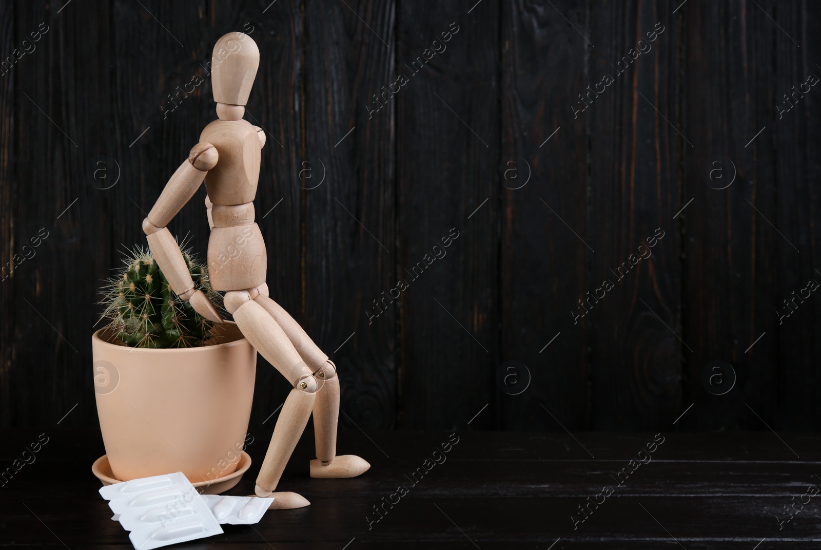 Photo of Wooden human figure, cactus and suppositories on black table, space for text. Hemorrhoid problems