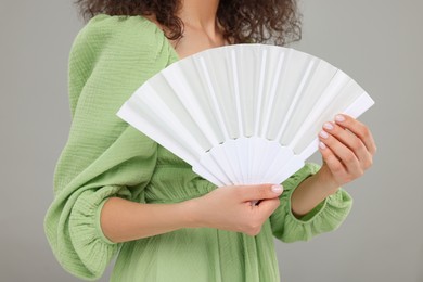 Photo of Woman holding hand fan on light grey background, closeup