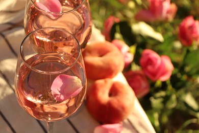Glasses of delicious rose wine with petals on white picnic blanket outside. Space for text