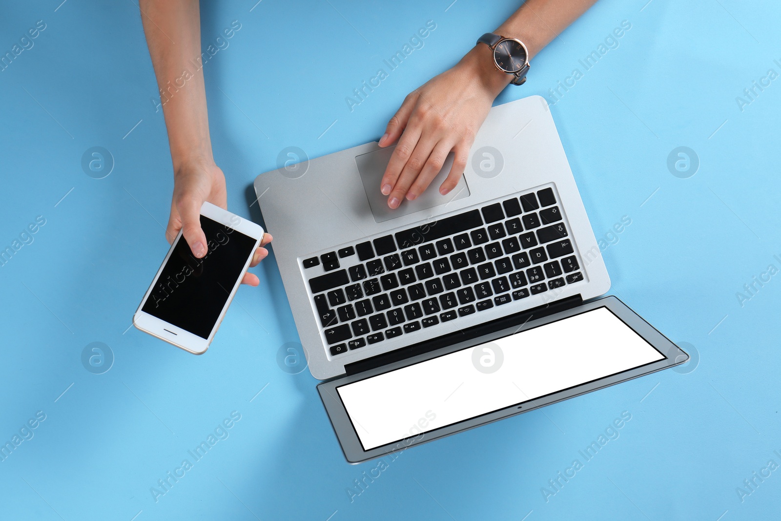 Photo of Young woman with mobile phone using laptop on light blue background, top view