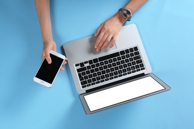 Photo of Young woman with mobile phone using laptop on light blue background, top view