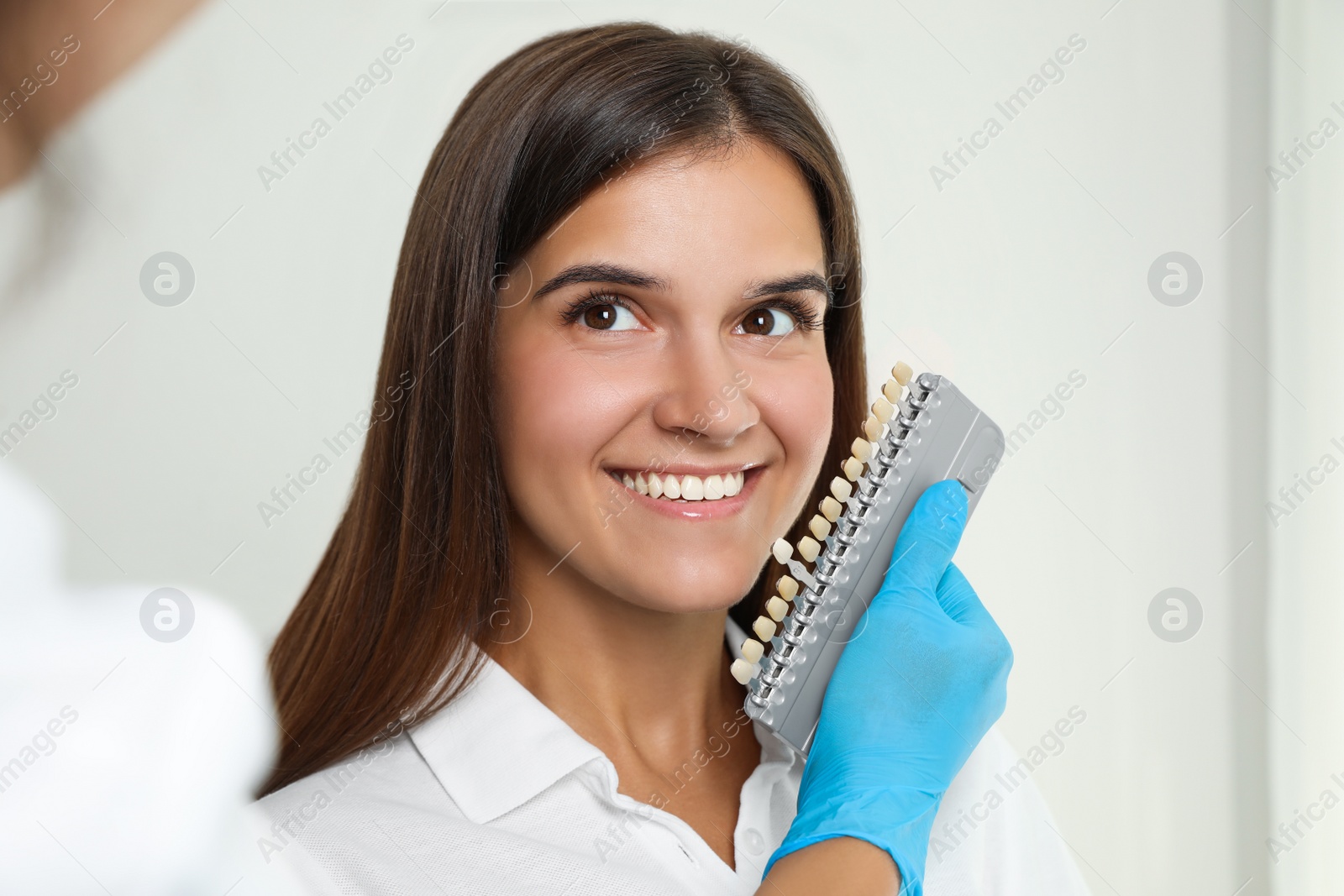 Photo of Doctor checking young woman's teeth color in clinic. Cosmetic dentistry