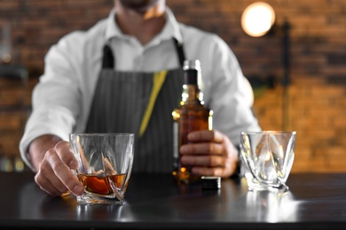 Photo of Bartender with glass and bottle of whiskey at counter in bar, closeup. Space for text
