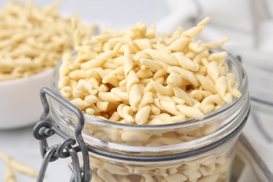 Uncooked trofie pasta in glass jar against blurred background, closeup