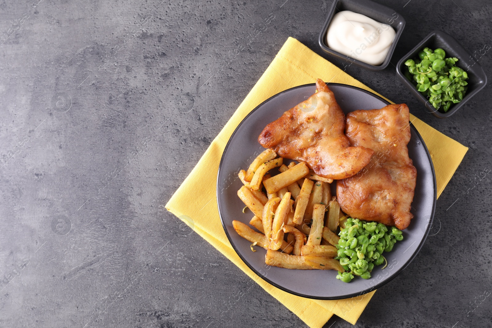 Photo of Tasty fish, chips, sauce and peas on grey table, flat lay. Space for text