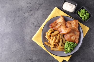 Tasty fish, chips, sauce and peas on grey table, flat lay. Space for text