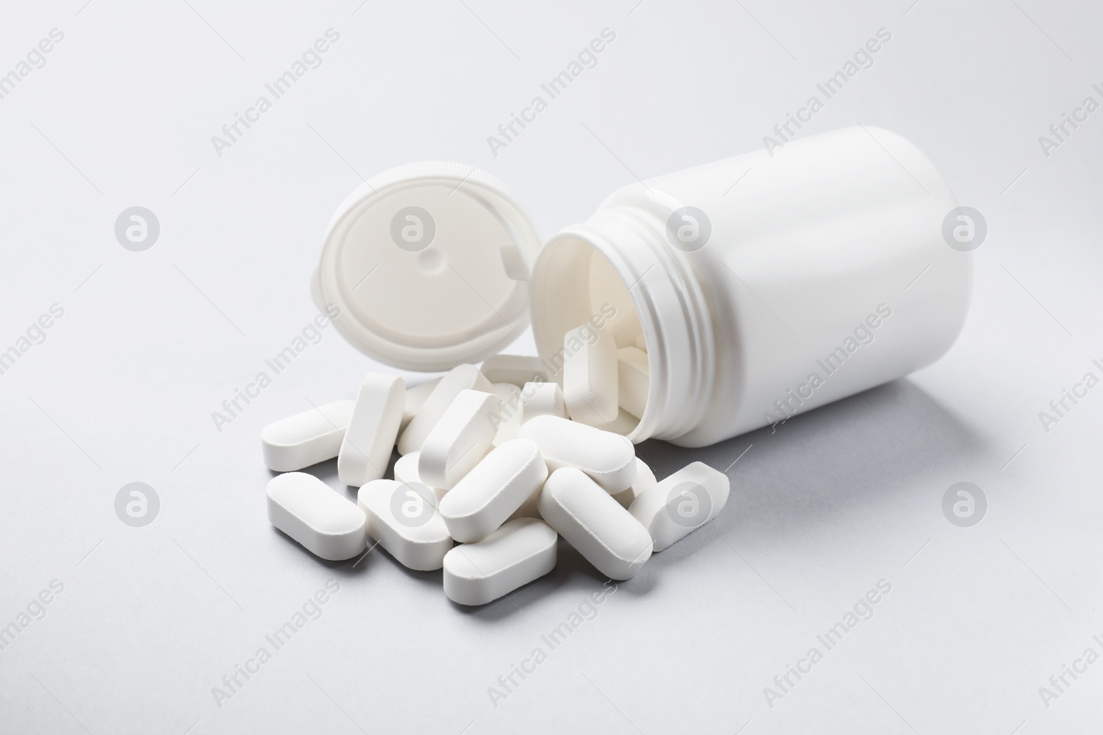 Photo of Bottle and vitamin capsules on light grey background