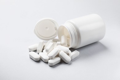 Photo of Bottle and vitamin capsules on light grey background